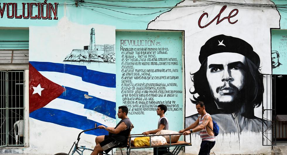 La gente transporta comida en un triciclo pasando junto a una pared pintada con la bandera de Cuba y un retrato del líder revolucionario argentino Ernesto "Che" Guevara, en La Habana el 27 de junio de 2023. (Foto de YAMIL LAGE / AFP).