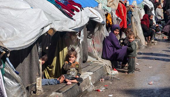 Una mujer y niños se sientan afuera de tiendas de campaña que albergan a palestinos desplazados en Rafah, en el sur de la Franja de Gaza, el 8 de febrero de 2024, en medio del conflicto en curso entre Israel y el grupo militante palestino Hamás. (Foto de Mohammed ABED / AFP)