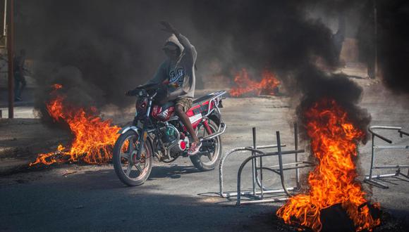 Una persona se transporta en motocicleta con incendios alrededor, cuando la tensión volvió este viernes a Puerto Príncipe con tiroteos entre la Policía y las bandas armadas. Foto: Johnson Sabin/EFE