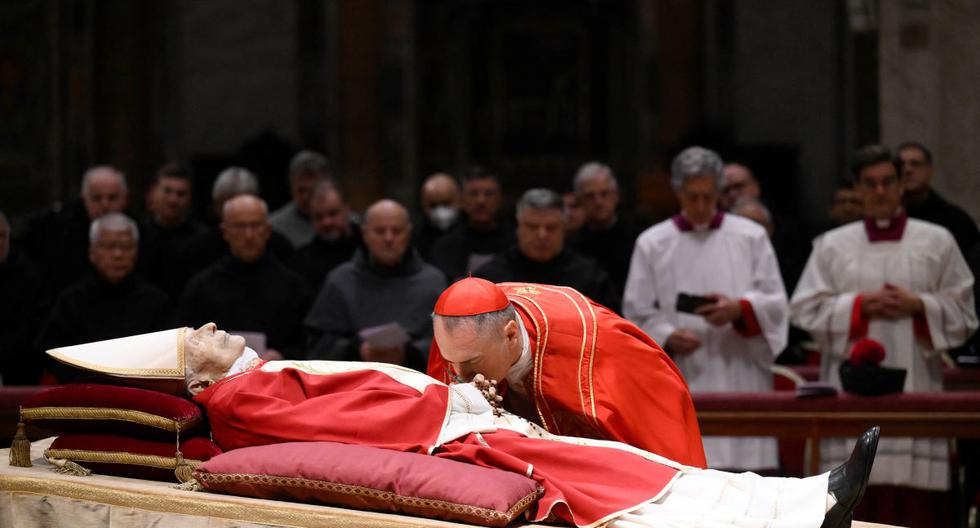Esta fotografía tomada el 2 de enero de 2023 por los medios del Vaticano muestra al cardenal Mauro Gambetti besando el cuerpo del papa emérito Benedicto XVI en la basílica de San Pedro. (HANDOUT / AFP / VATICAN MEDIA).