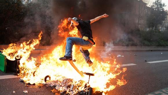 Un manifestante monta una patineta sobre contenedores de basura en llamas durante una manifestación después de que el gobierno aprobara una reforma de las pensiones en el parlamento sin votación, utilizando el artículo 49.3 de la constitución, en Toulouse, en el sur de Francia, el 28 de marzo de 2023. (Foto de CHARLY TRIBALLEAU / AFP)