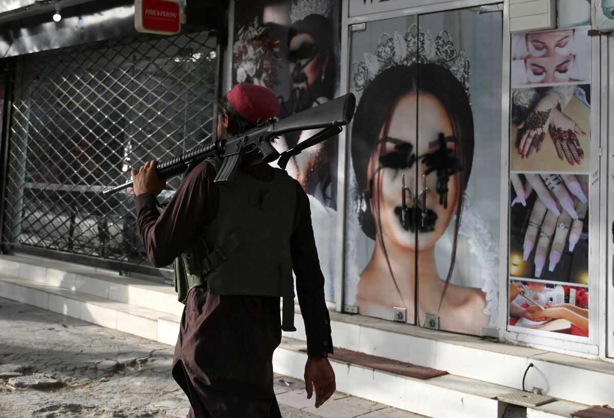 A Taliban fighter walks past a beauty salon with images of women disfigured with spray paint in Shar-e-Naw, Kabul, on August 18, 2021. (Wakil KOHSAR / AFP)