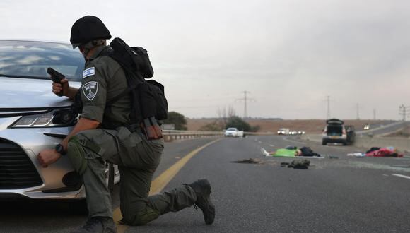 Un soldado de Israel se refugia detrás de un automóvil mientras mira los cuerpos en una carretera principal cerca del kibutz Gevim, cerca de la frontera con Gaza el 7 de octubre de 2023. (Foto de Oren ZIV / AFP).